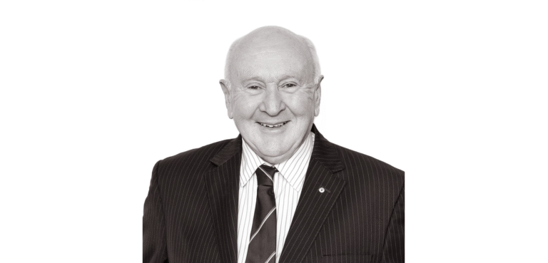 Senior lawyer smiling, wearing a striped suit and tie, against a plain background.