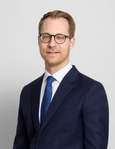 Lawyer in suit and glasses posing against a neutral background.
