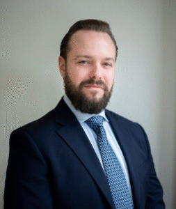 Lawyer in a business suit with a beard, smiling against a neutral background.