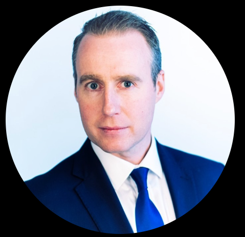 Professional man in a suit with blue tie, posing for a portrait against a light background.