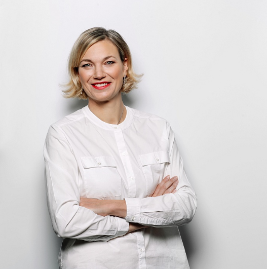 Female lawyer smiling with arms crossed, dressed in a white shirt, in a neutral studio setting.