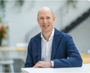 Business professional smiling while seated at a desk in a modern office setting.