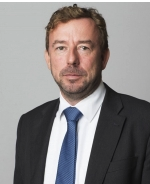 Lawyer in a suit, looking directly at the camera, in a neutral professional setting.