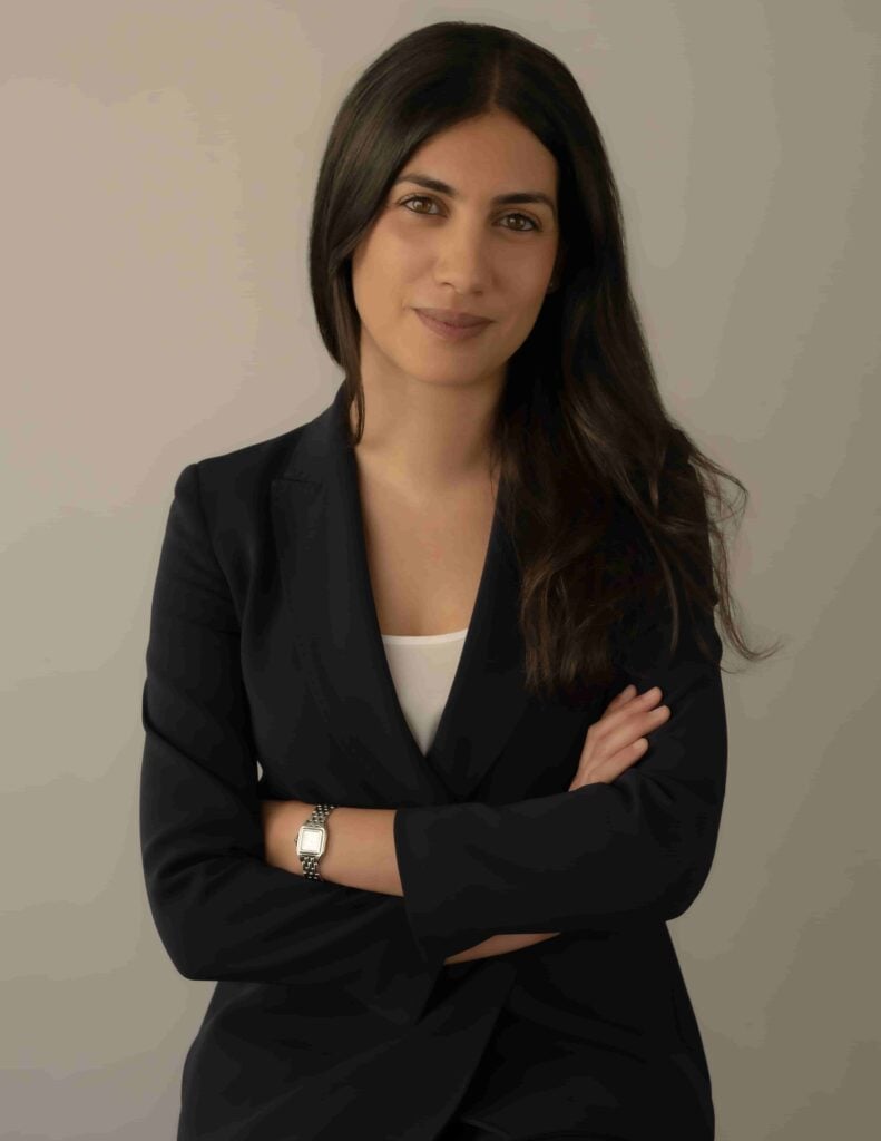 Female attorney standing with arms crossed, wearing a black suit against a neutral background.