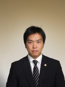 Lawyer in formal suit posing against a neutral background with a serious expression.