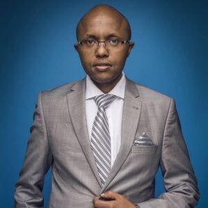 Lawyer in gray suit with striped tie, standing confidently against a blue background.