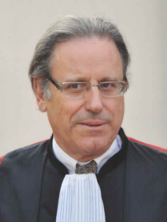 Judge in formal robe and glasses, posing for a portrait against a neutral background.