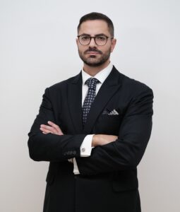 Lawyer in a suit, arms crossed, presenting a confident demeanor against a plain background.