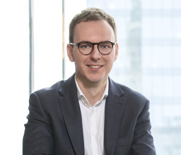 Lawyer smiling and seated in a modern office with large windows and a professional appearance.