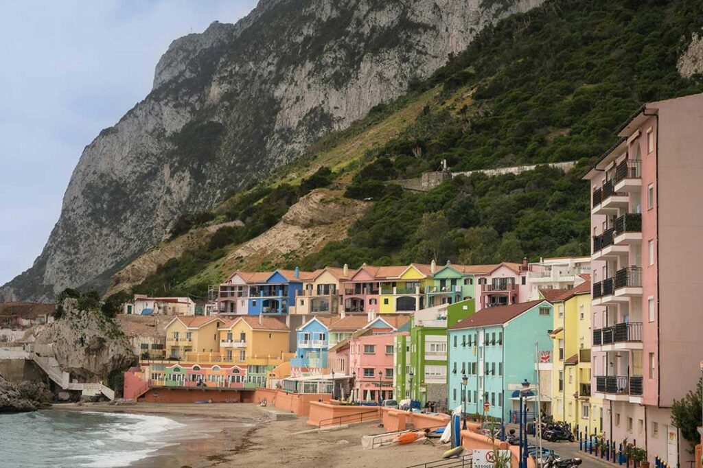 Colorful residential buildings along a beach with a mountain backdrop in a coastal setting.