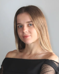 Young woman with long hair posing against a plain background, wearing an off-the-shoulder black top.