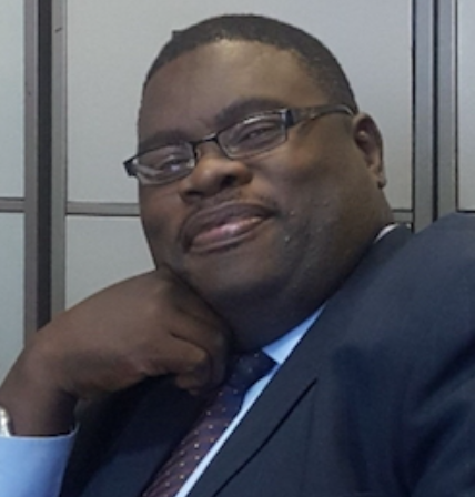 Lawyer smiling while sitting at desk, with hand on chin in a professional office setting.