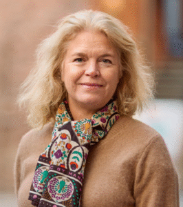 Legal professional with blonde hair, wearing a patterned scarf, smiling outdoors in a law-related environment.