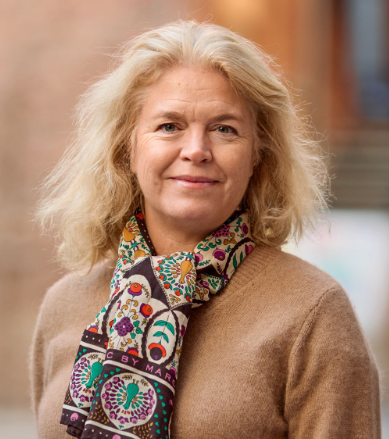 Legal professional with blonde hair, wearing a patterned scarf, smiling outdoors in a law-related environment.