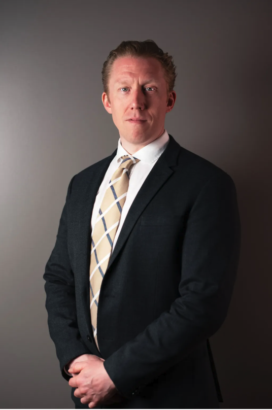 Attorney posing confidently in a suit against a neutral backdrop.