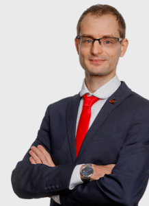 Lawyer in a suit with arms crossed, wearing glasses, professionally posed for a legal profile.