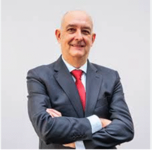 Lawyer standing with arms crossed, smiling, in a neutral setting suitable for professional portraits.
