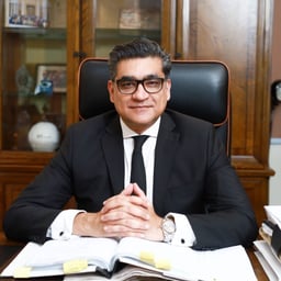 Attorney seated at desk with hands clasped, surrounded by legal documents in professional office setting.
