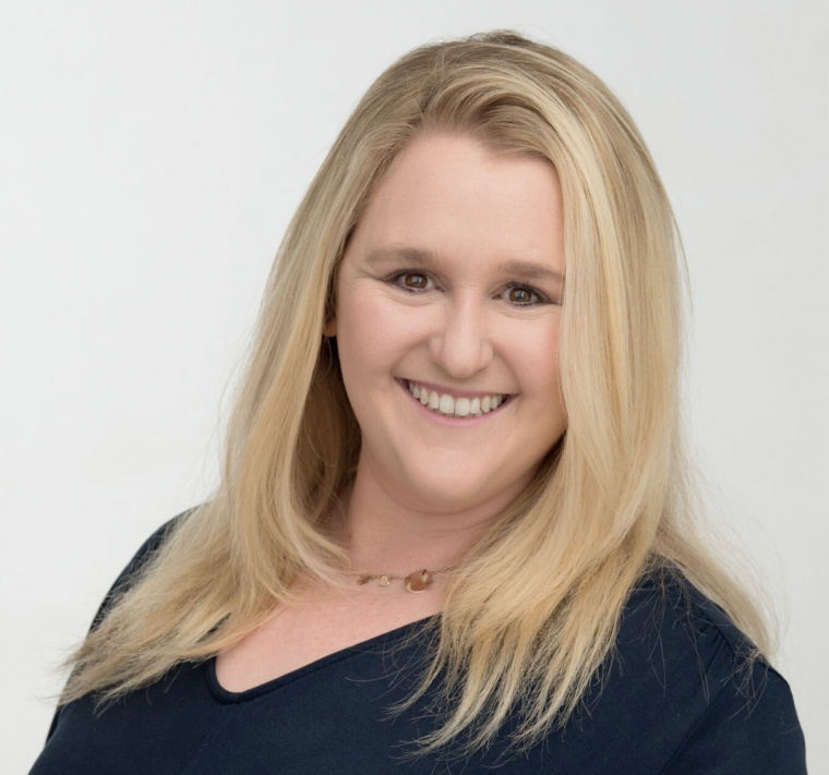 Professional with blonde hair smiling, in a dark shirt, in a neutral setting suitable for a legal profile.