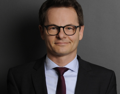 Lawyer in professional attire, smiling, against a plain background.