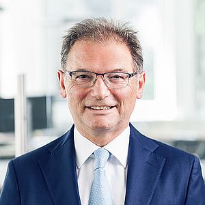 Male lawyer smiling in a professional suit, standing in an office environment with a modern backdrop.