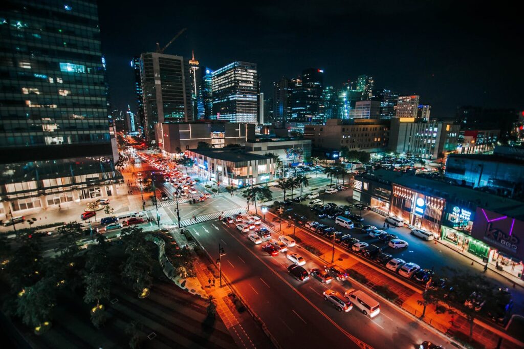 Nighttime cityscape showing busy streets with traffic and illuminated buildings in an urban setting.