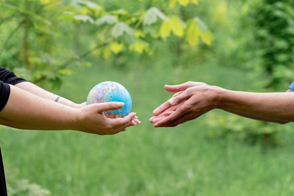 Hands exchanging a small globe in a green outdoor setting, symbolizing collaboration and global awareness.