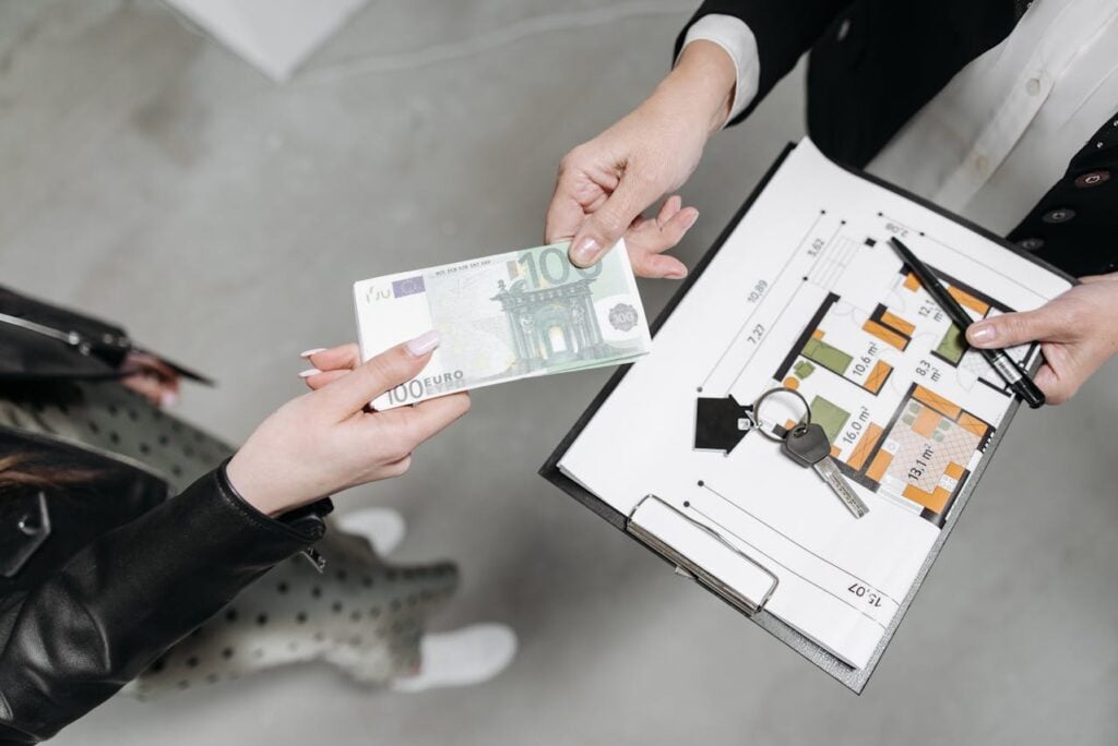 Person handing cash while receiving a property layout with keys, indicating a real estate transaction.